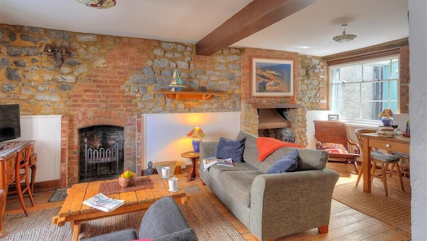 A cozy living room with a stone fireplace, wooden furniture, and a dining area. - Bedrock (Lyme Regis)
