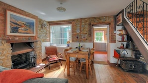 A cozy dining area with a stone fireplace, wooden dining table, and chairs. A staircase with a wrought iron railing is visible on the right. - Bedrock (Lyme Regis)