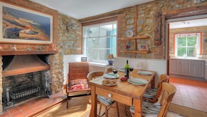 A cozy dining area with a stone fireplace, wooden furniture, and a large window providing natural light. - Bedrock (Lyme Regis)