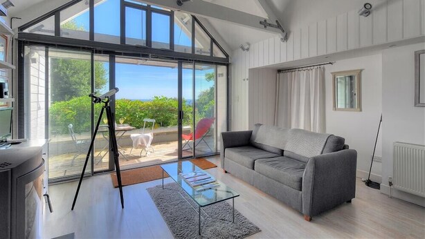 Ein modernes Wohnzimmer mit Glastür zum Balkon, einem grauen Sofa, einem Glastisch und einem Stativ.