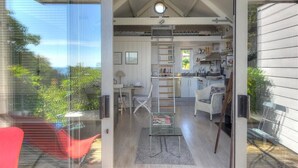 Ein modernes Interieur mit einer Loft-Küche, einem Essbereich und einem Wohnraum mit Glaswand mit Blick auf Grünflächen.