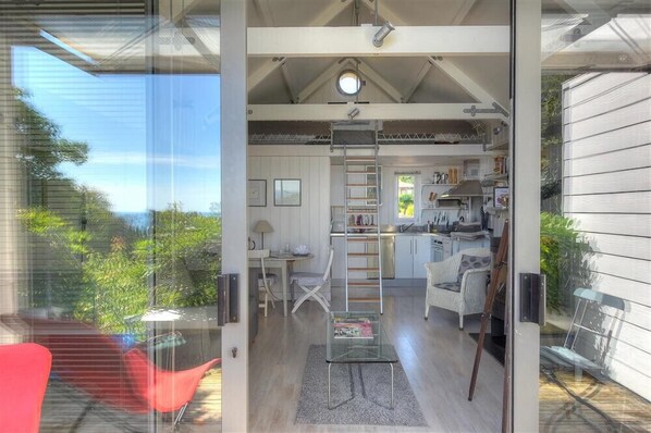 A modern interior with a loft-style kitchen, a dining area, and a living space with a glass wall overlooking greenery. - Little West Hill Studio (Lyme Regis)