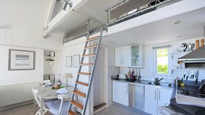 Eine moderne Küche mit weißen Schränken, einer Edelstahlspüle und einem eingebauten Backofen. Eine Holzleiter lehnt an der Wand, und ein Fenster sorgt für natürliches Licht.