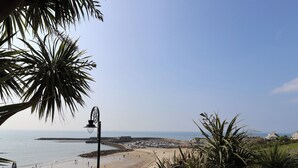 A beach with a clear view of the sea, a sandy shore, and a distant rocky outcrop. - Greystones Flat (Lyme Regis)