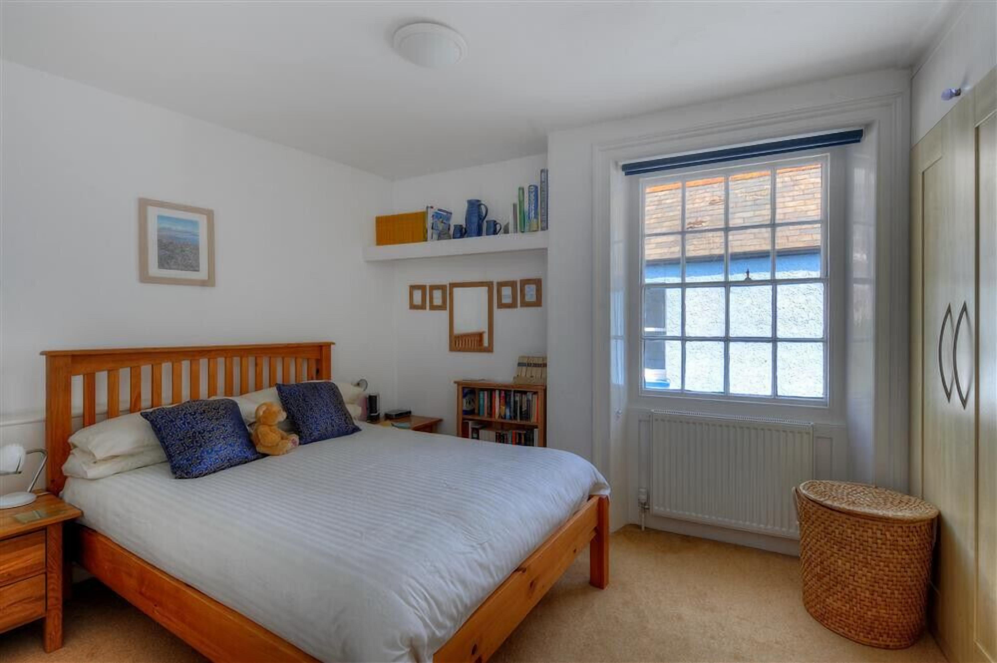 A bedroom with a wooden bed, a bedside table, a bookshelf, a window with blinds, and a radiator.