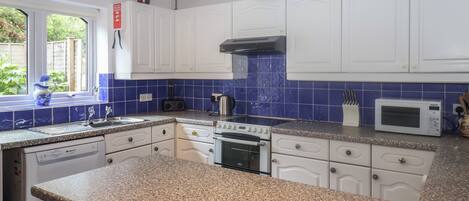 Une cuisine avec des meubles blancs, des plans de travail en granit, une cuisinière, un four à micro-ondes et une fenêtre donnant sur un paysage verdoyant.