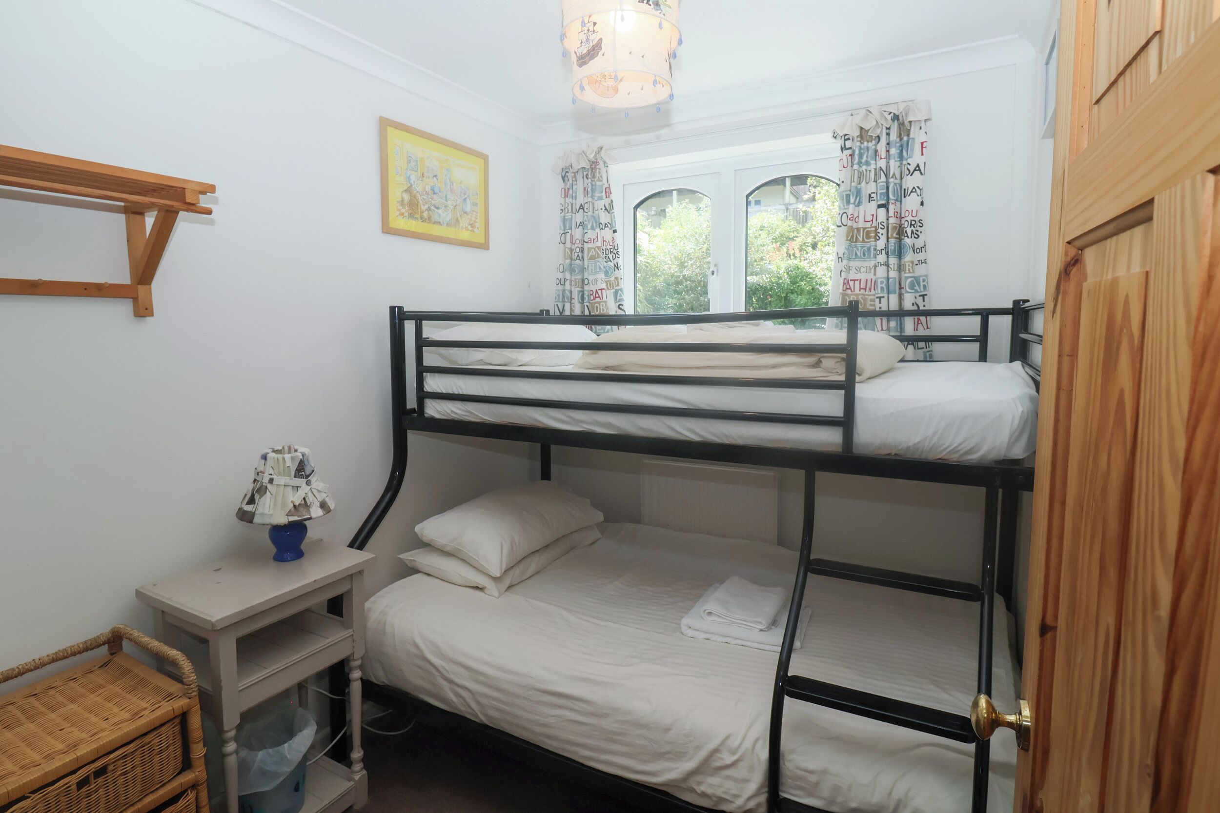 A bunk bed room with a small table, a lamp, and a window with curtains.