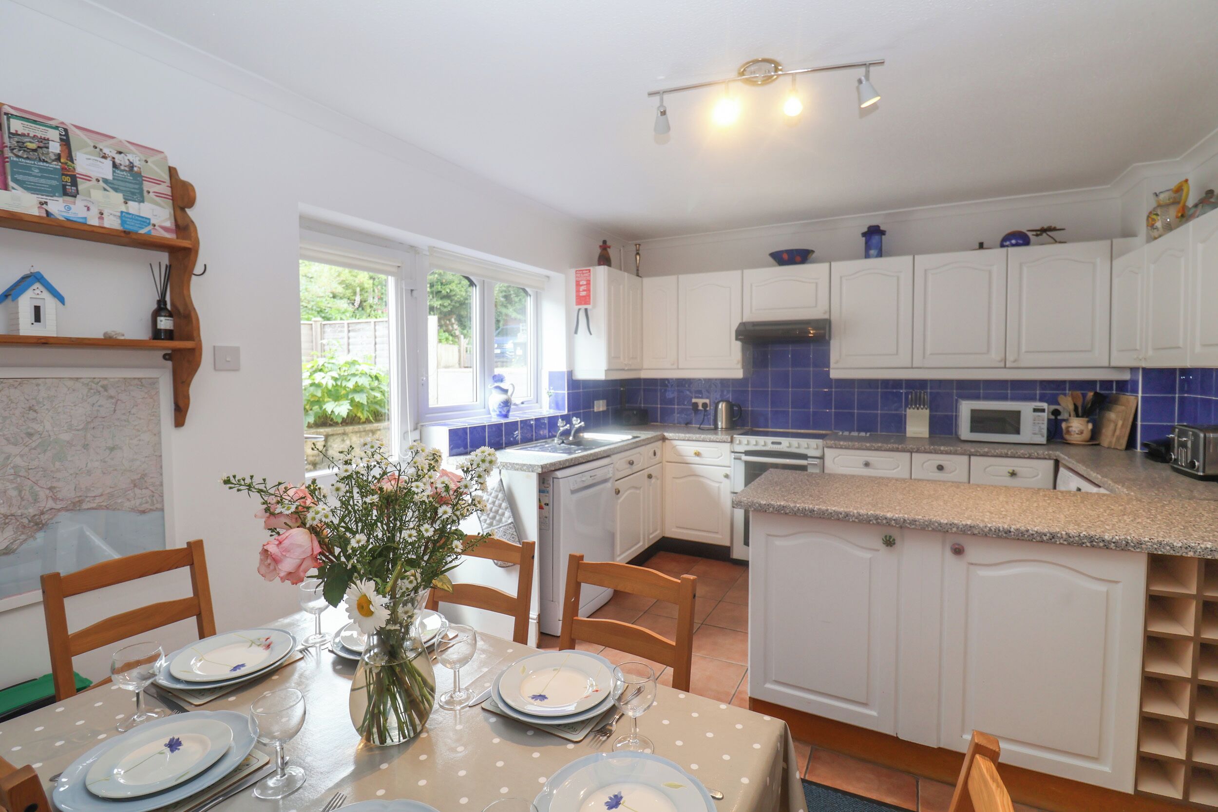 A well-lit kitchen with white cabinets, a blue tiled backsplash, and a dining area with a table set for four.