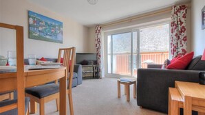 A living room with a sofa, a dining table, and a TV. - 4 Bay View Court (Lyme Regis)