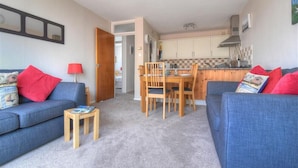 A living room with a blue sofa, a wooden dining table, and a kitchen in the background. - 4 Bay View Court (Lyme Regis)