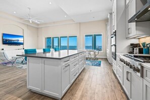 Une cuisine moderne dotée d’un grand îlot central, de meubles blancs et offrant une vue sur l’océan.