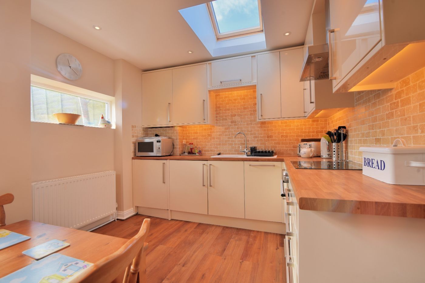 A modern kitchen with a skylight, white cabinets, a microwave, and a bread container.