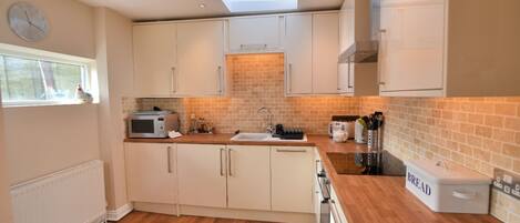 A modern kitchen with white cabinets, a brick backsplash, and a skylight.