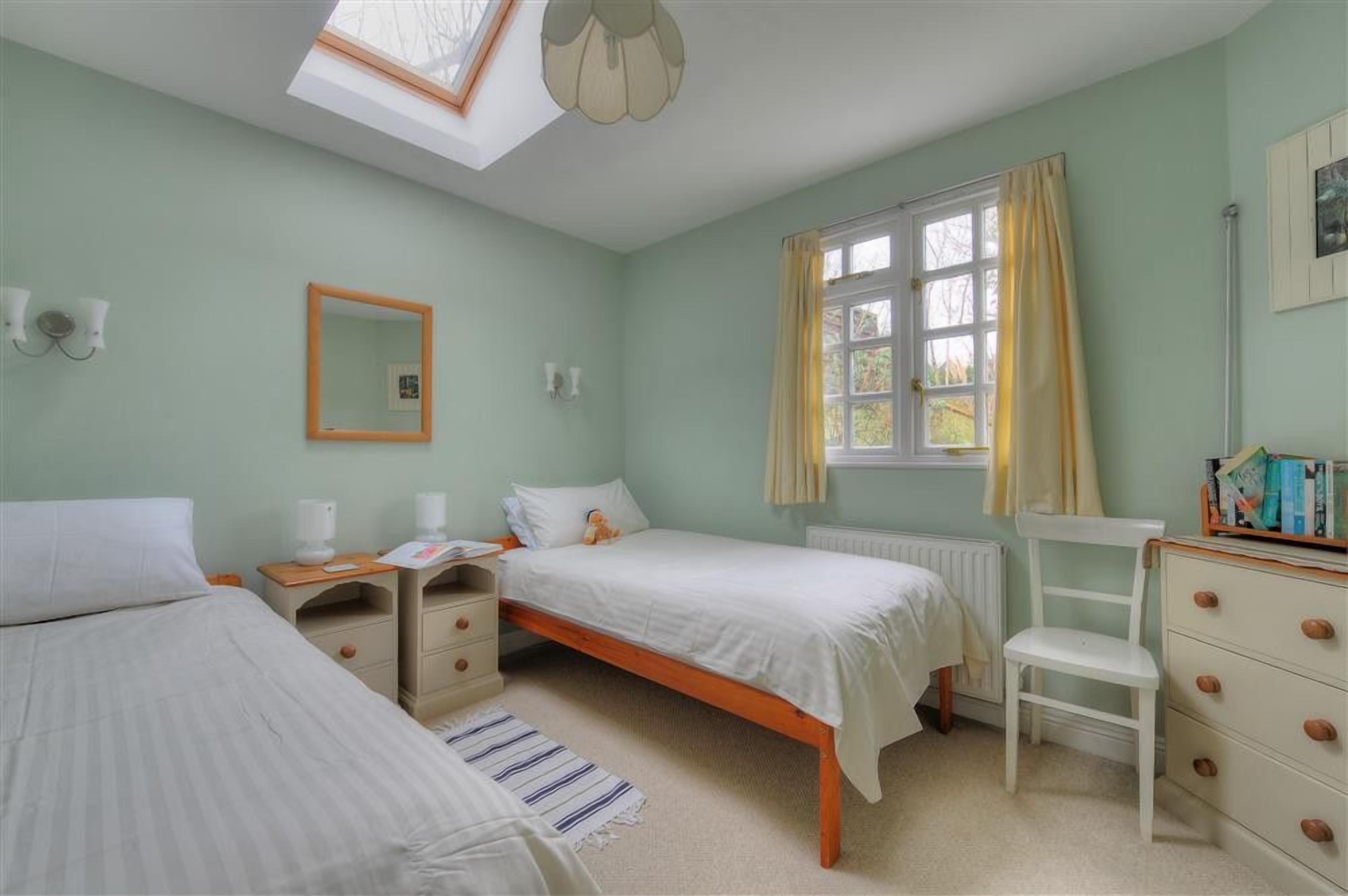 A bedroom with two single beds, a desk, a chair, a radiator, and a window with curtains.
