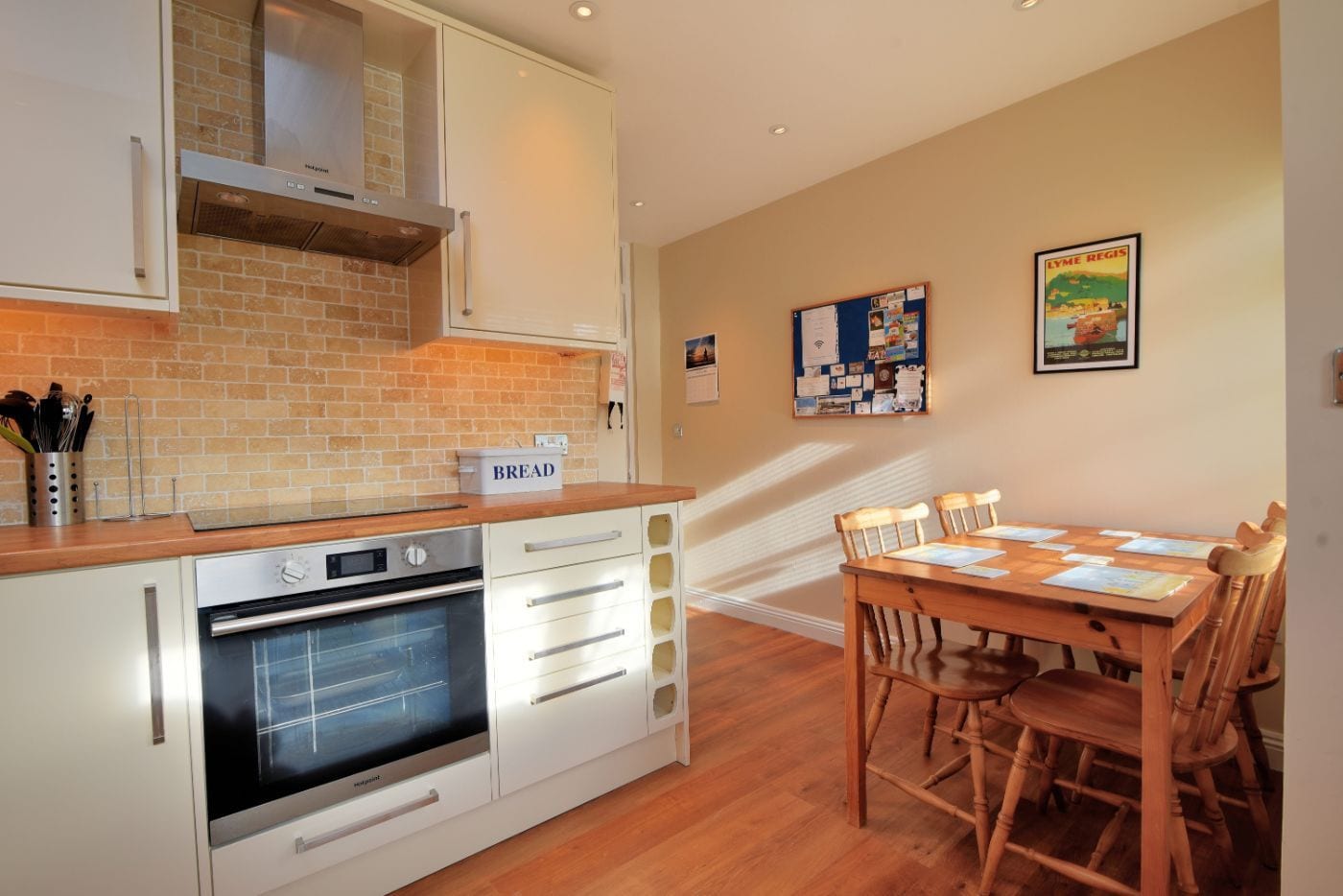 A modern kitchen with white cabinetry, a brick backsplash, and a dining area with wooden chairs and a table.