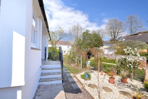 A white building with a stone staircase leading to a garden area with potted plants and a small tree. - The Bolthole (Lyme Regis)
