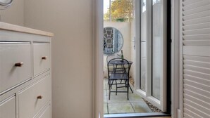 En vy genom en skjutdörr i glas som leder ut till en uteplats med ett bord och stolar, en dekorativ fläkt och en väggmonterad luftkonditioneringsanläggning.