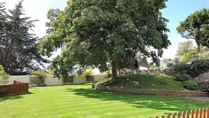 A well-maintained lawn with a wooden fence, a large tree, and a stone wall in the background. - 5 Coram Tower (Lyme Regis)