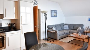 A modern kitchen with white cabinets, a coffee maker, and a dining area with a table and a sofa. - 5 Coram Tower (Lyme Regis)
