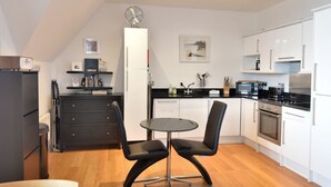 A compact kitchen with a dining area, featuring a small round table, two chairs, a refrigerator, a microwave, and a stove. - 5 Coram Tower (Lyme Regis)