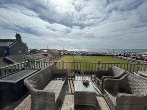 A balcony with wicker furniture overlooking a grassy area and a parking lot.