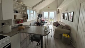 A kitchen with a dining area, a sofa, and a view of the outside. - 8 Bowling Green Chalets (Lyme Regis)