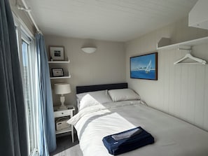 Ein Schlafzimmer mit einem Bett, einem Nachttisch, einer Lampe, einem Bilderrahmen, einem Handtuch und einem Kleiderständer.
