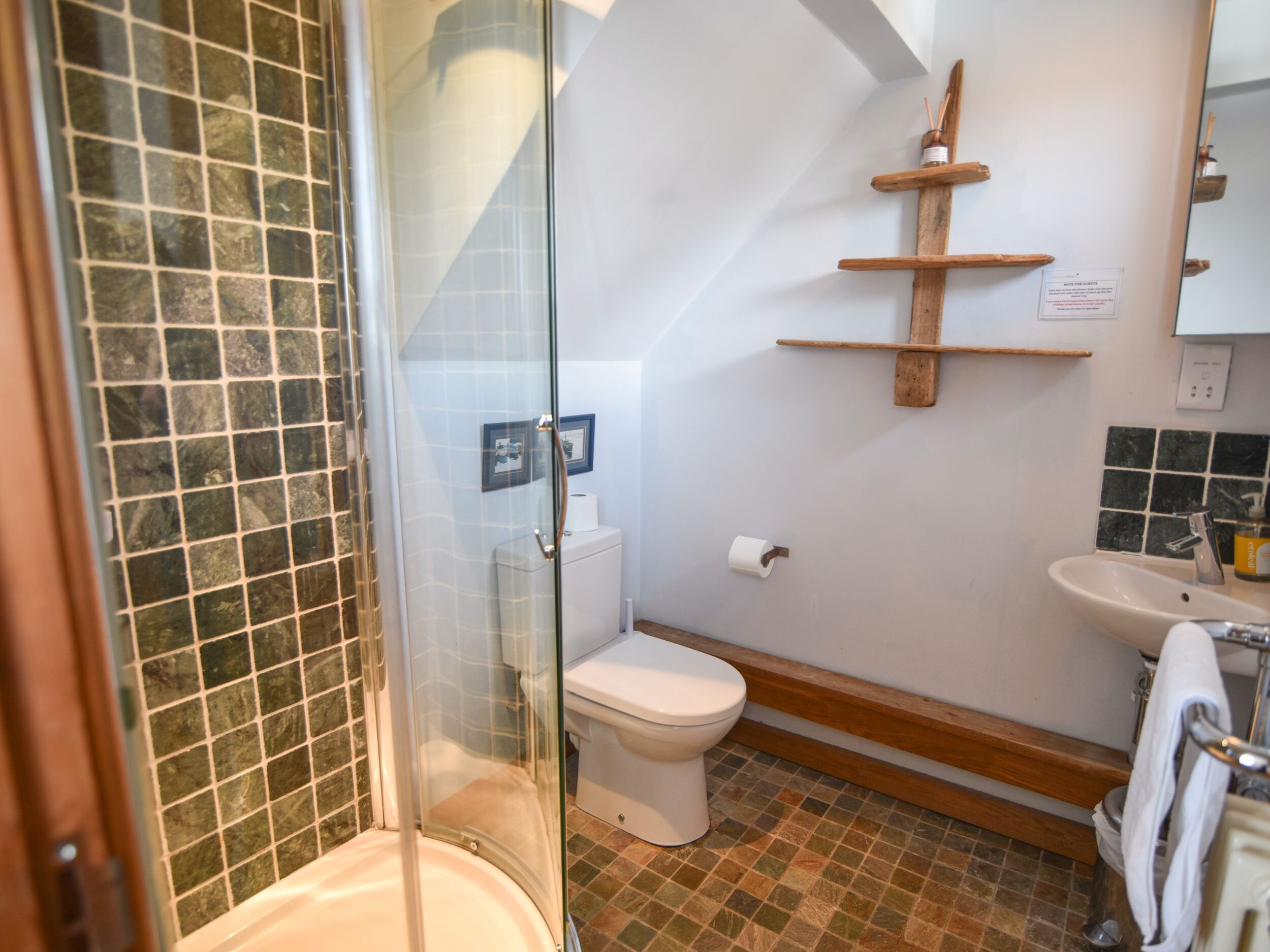 A bathroom with a glass-enclosed shower, a toilet, a sink, and a wooden shelf.