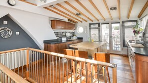 A modern kitchen with wooden beams, a central island, and bar stools. - The Lookout (Lyme Regis)