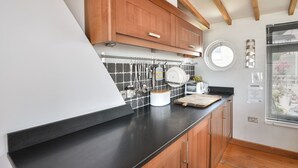 A kitchen with wooden cabinets, a black countertop, and a tiled backsplash. - The Lookout (Lyme Regis)