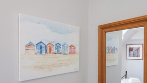 Une chambre avec un lit, une table de chevet et un tableau coloré représentant des cabanes de plage, accroché au mur.