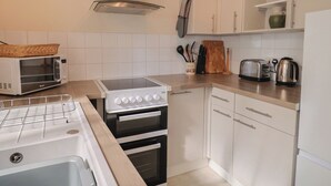 A kitchen with a microwave, stove, oven, and a clock on the wall. - 3 Dolphin Cottages (Lyme Regis)