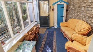A conservatory with a sofa, chairs, a small table, and a blue door. - 3 Dolphin Cottages (Lyme Regis)
