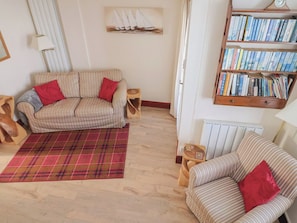 Ein Wohnzimmer mit gestreiften Sofas, einem karierten Teppich, einem Bücherregal und einer Wandablage mit Büchern.