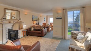 A living room with a fireplace, leather sofas, a dining area, and a large window with curtains. - The Portland Suite (Lyme Regis)