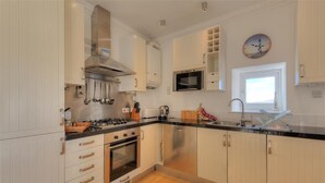 A modern kitchen with white cabinets, stainless steel appliances, and a black countertop. - The Portland Suite (Lyme Regis)