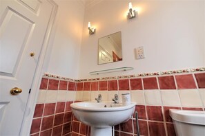 A bathroom with a white sink, two wall-mounted lights, a mirror, and a tiled backsplash. - The Portland Suite (Lyme Regis)