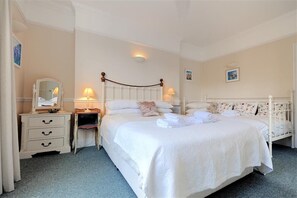 A neatly arranged bedroom with a large bed, bedside tables, a mirror, and wall-mounted lamps. - The Portland Suite (Lyme Regis)