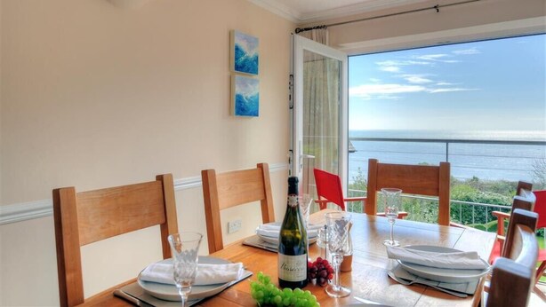 A dining table set for four with a bottle of wine, glasses, and a view of the sea. - The Portland Suite (Lyme Regis)