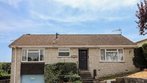 Uma casa de dois andares com telhado de telhas, porta da garagem azul e um pequeno jardim frontal.