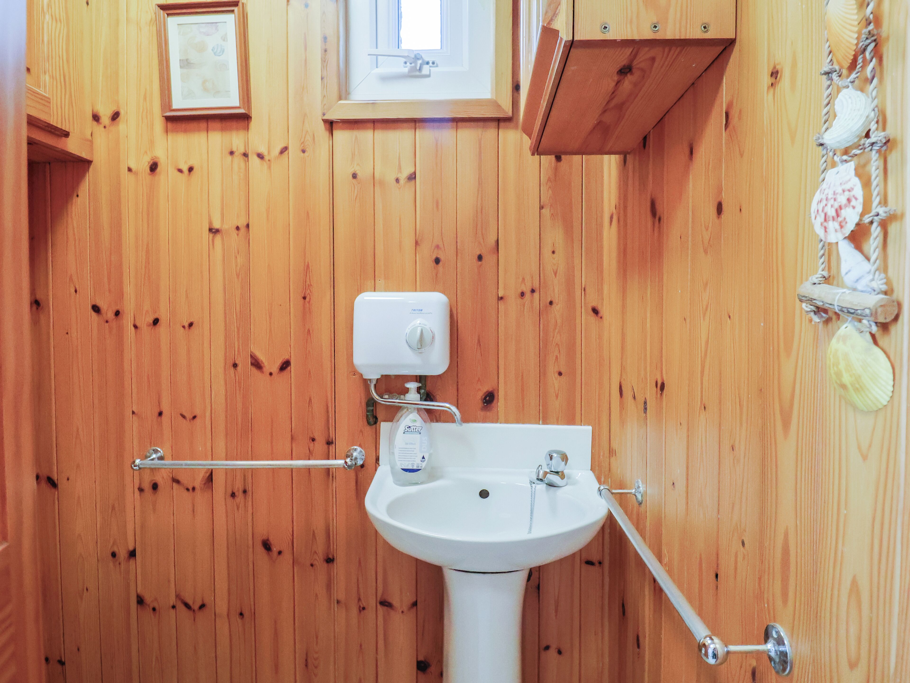 Ein Badezimmer mit Holzverkleidung, einem weißen Waschbecken, einer Toilette und einem Fenster über dem Waschbecken.