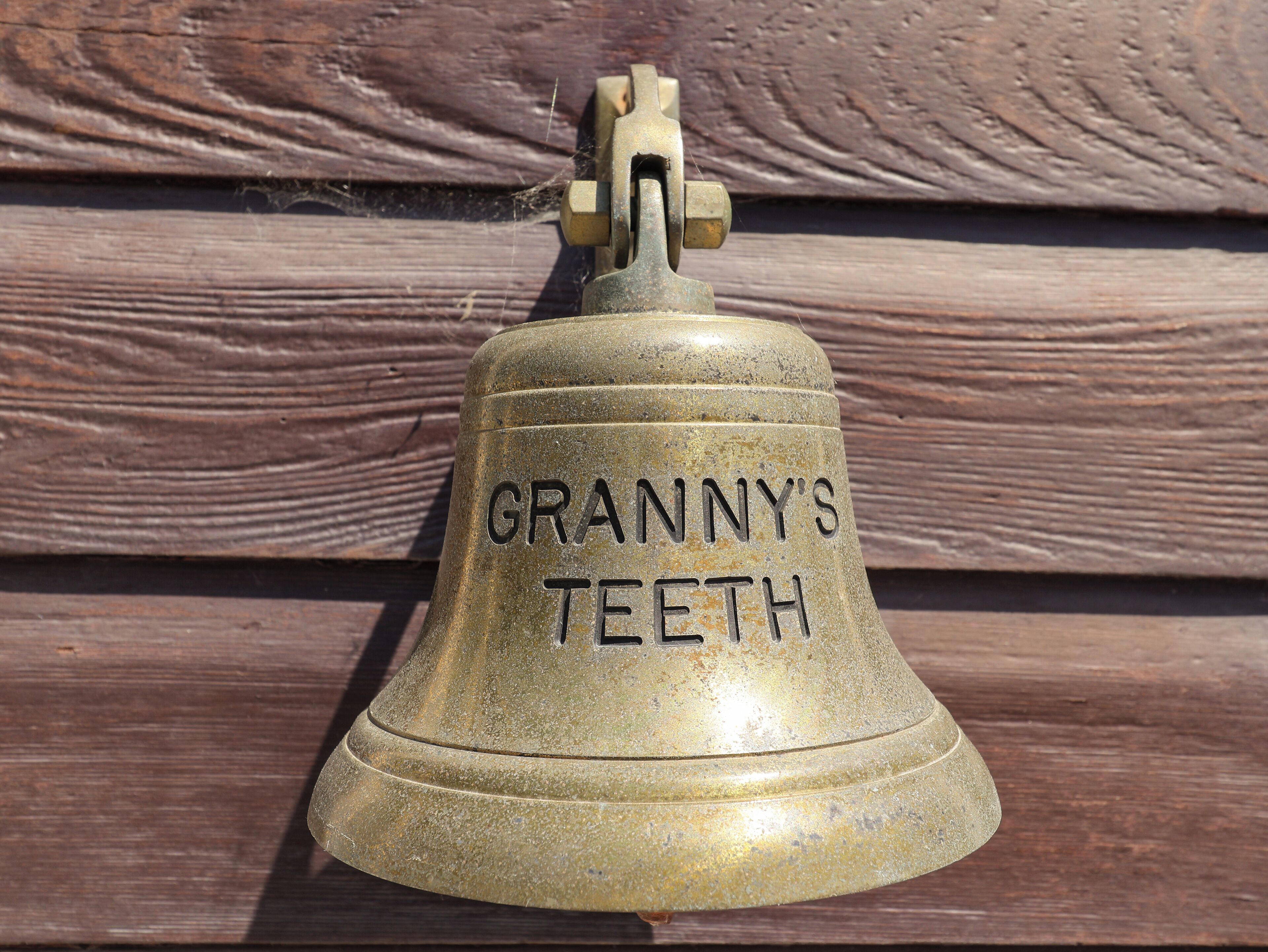 A brass bell with the inscription "GRANNY'S TEETH" mounted on a wooden wall.