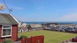 A coastal view with a grassy lawn, a red building, and a marina with boats. - Granny's Teeth (Lyme Regis)