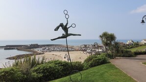 A coastal view with a sculpture of a figure holding rings, a beach, and a marina in the background. - Granny's Teeth (Lyme Regis)
