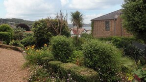 A garden with various plants and a brick building. - The Apartment at Queen Anne's Lodge (Lyme Regis)