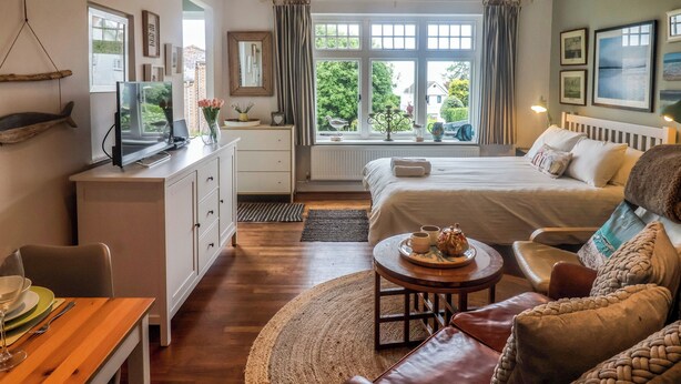 A well-lit bedroom with a bed, bedside table, and a view of greenery outside. - The Apartment at Queen Anne's Lodge (Lyme Regis)