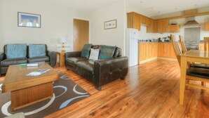 A modern living room with a sofa, coffee table, and a dining area with a table and chairs. - 8 Buckfields (Lyme Regis)