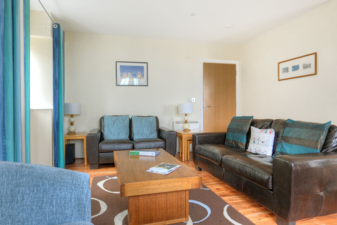 A living room with a sofa, a coffee table, and a chair. There is a door and a framed picture on the wall.