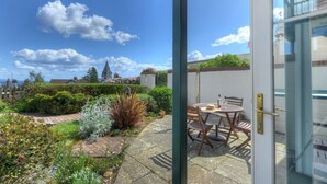 A garden patio with a table and chairs, a clear sky, and a building in the background. - 8 Buckfields (Lyme Regis)
