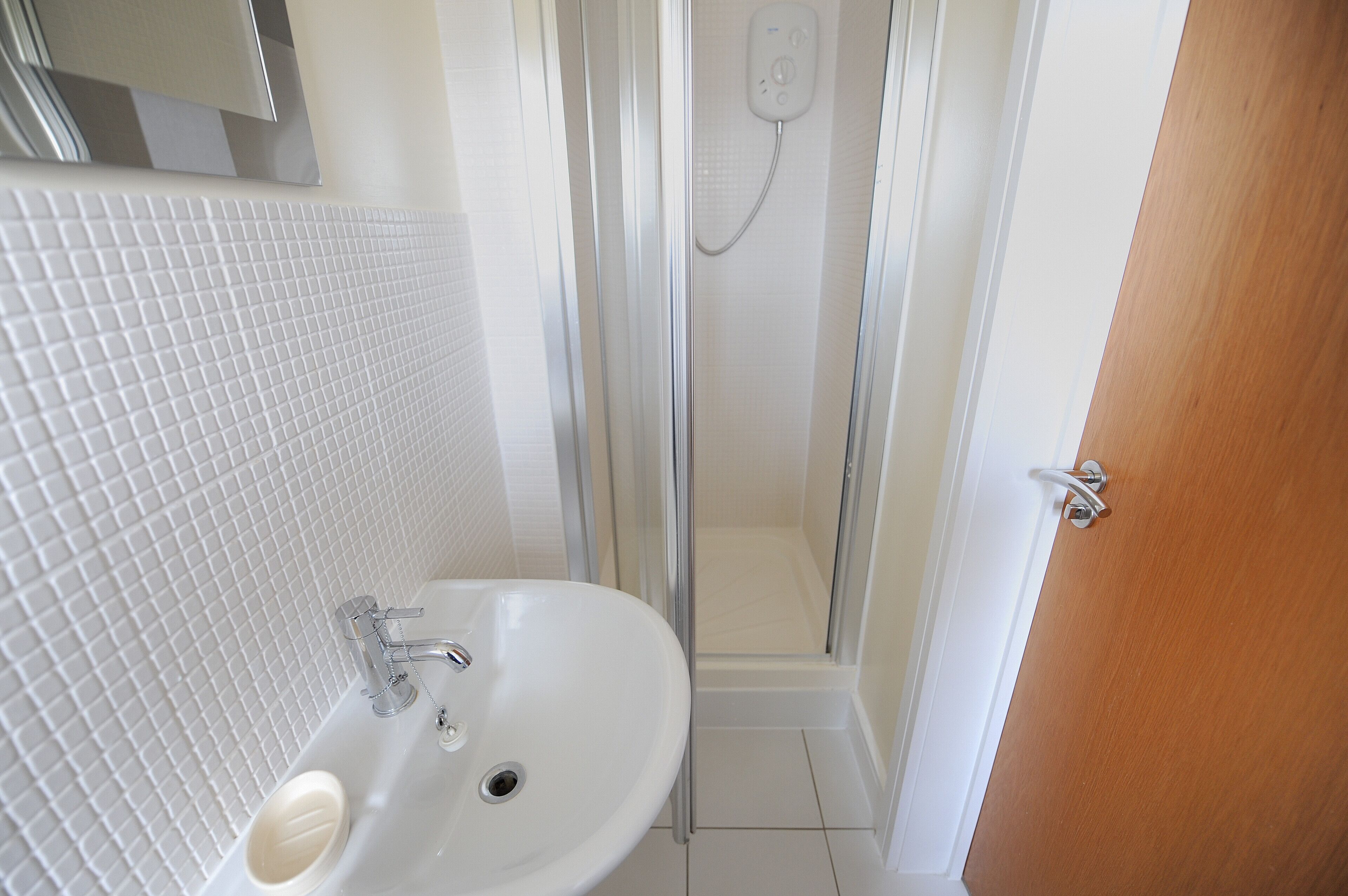 A bathroom with a white sink, a glass shower enclosure, and a wooden door.